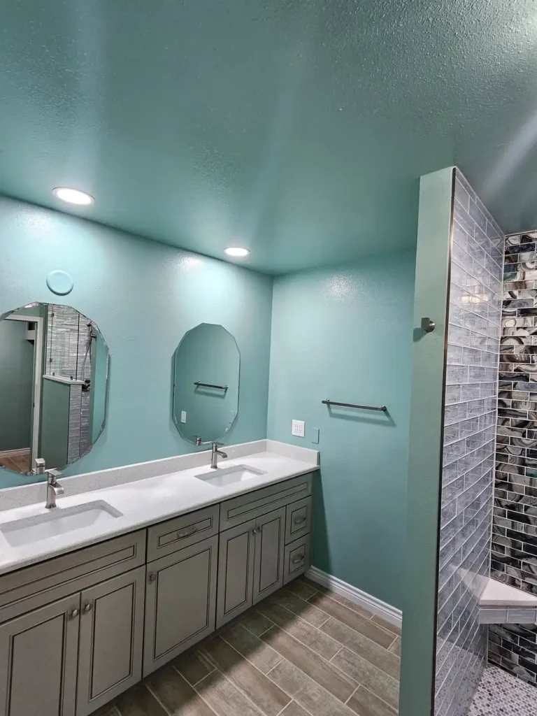 Modern bathroom with a double-sink vanity, quartz countertop, and wall-mounted mirrors. The space features light blue walls, recessed lighting, wood-look floor tiles, and a tiled walk-in shower.