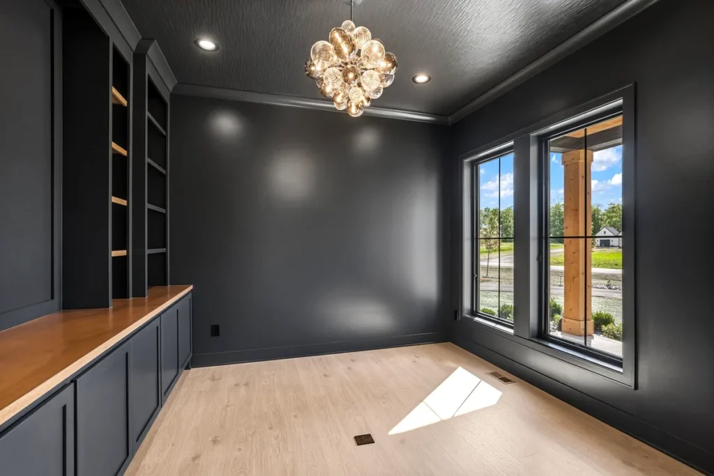 A classic home office addition with rich dark walnut built-in cabinetry, open display shelving, a solid wood executive desk, leather chair, and guitar display cases on the wall — all tied together by dark hardwood floors and warm wood ceiling fan. A refined and personalized Philadelphia home addition ideal for a luxury home office.